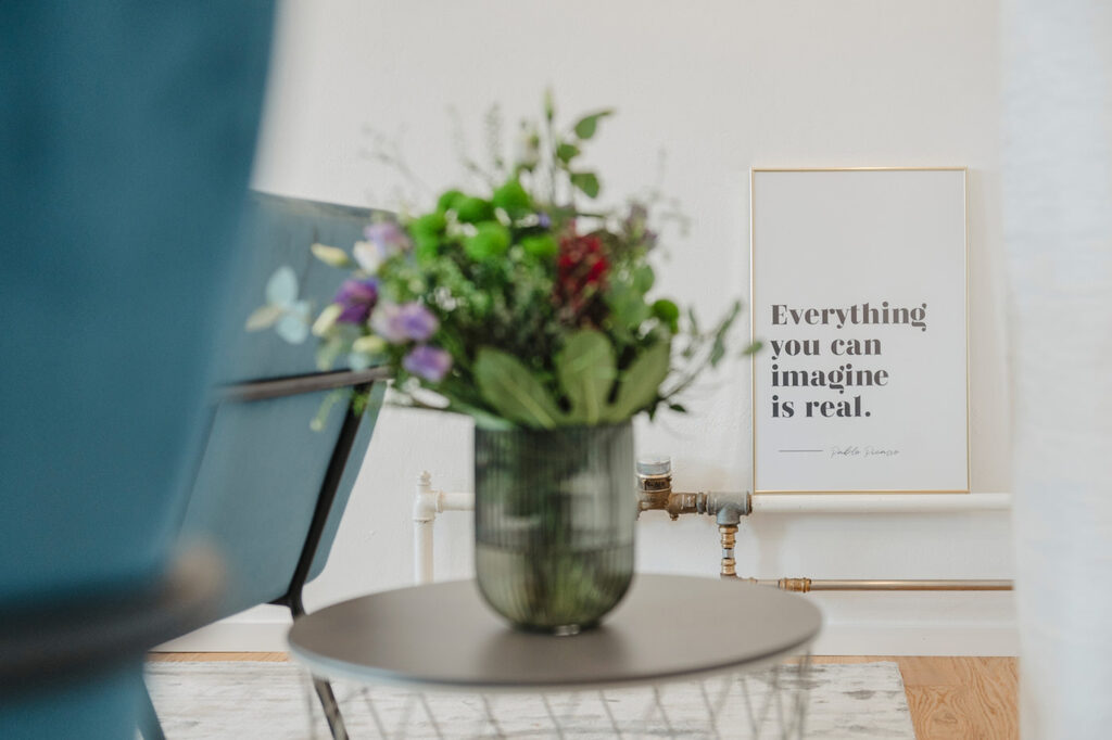 Blumenstrauß auf einem Beistelltisch, dahinter ein gerahmtes Bild mit dem Satz »Everything you can imagine is real«