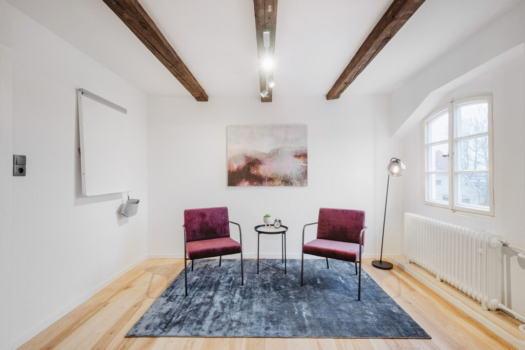 Kleiner Coachingraum mit zwei roten Sesseln, Beistelltisch und Whiteboard