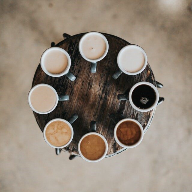 Nathan Dumlao on Unsplash_quad Neun Kaffeetassen im Kreis auf einem runden Holztisch, von oben fotografiert